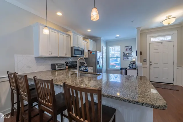 a kitchen with stainless steel appliances granite countertop a stove top oven a sink a dining table and chairs