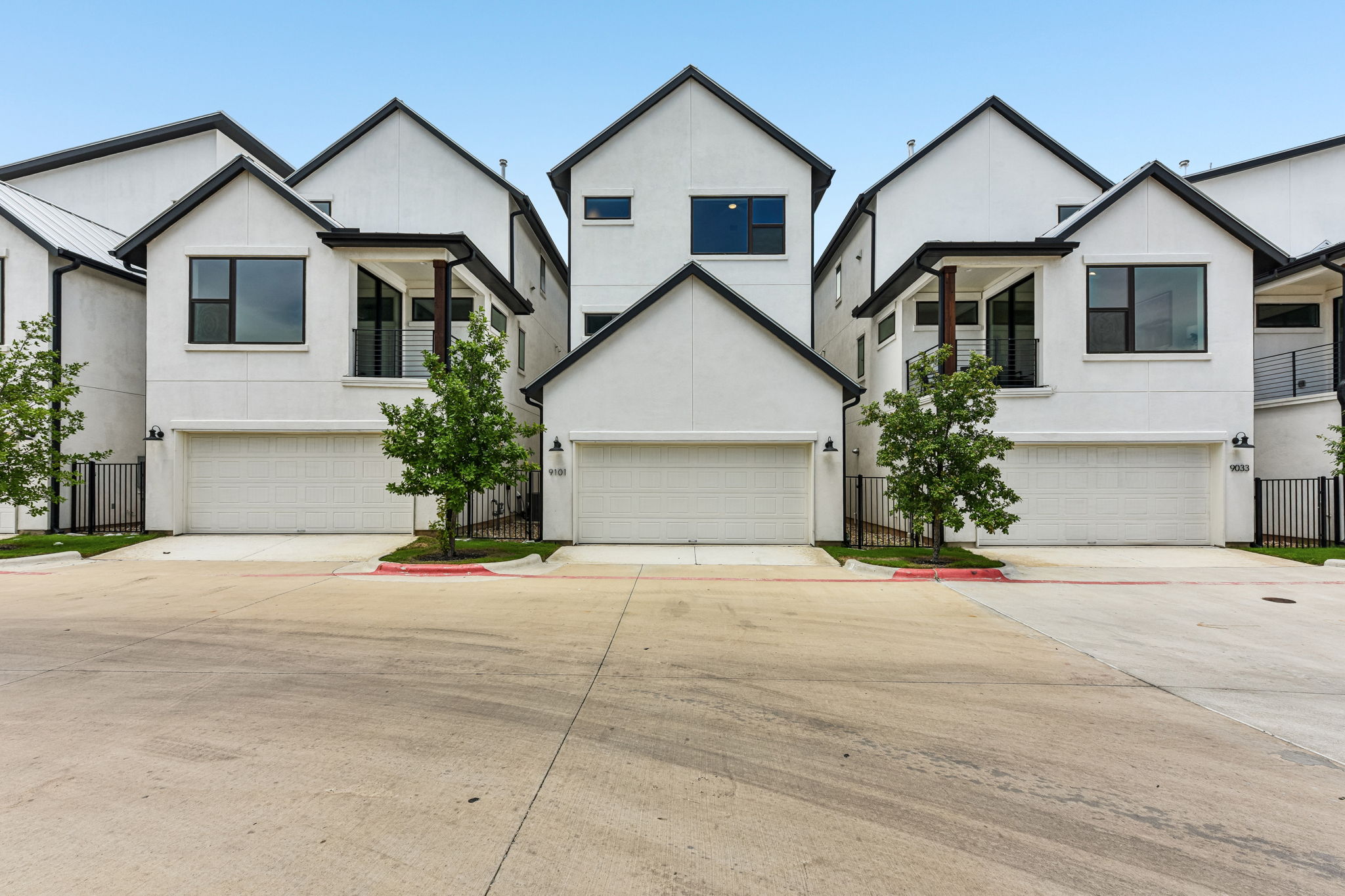 9101 Cattle Baron Path Austin, TX 78747 - Photo 40 of 40 Modern townhomes showcasing crisp white facades and individual attached garages line the street.