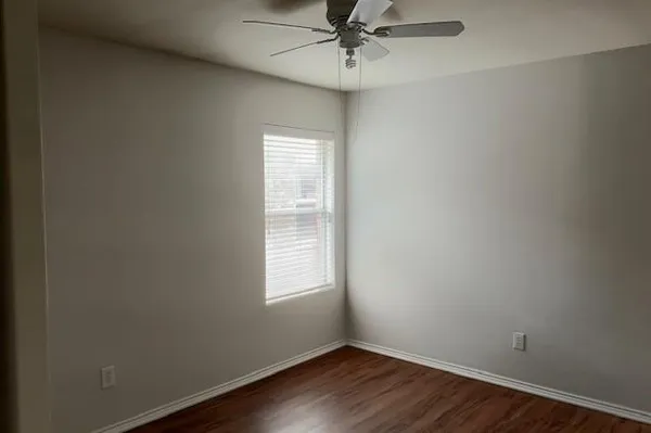 an empty room with wooden floor fan and windows