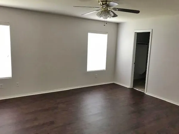 an empty room with wooden floor chandelier fan and windows