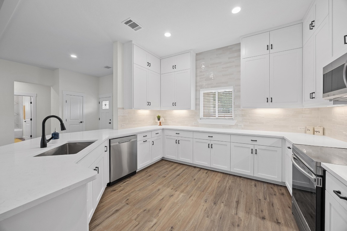 17701 Village Drive Dripping Springs, TX 78620 - Photo 12 of 36 a large white kitchen with stainless steel appliances granite countertop a stove a sink dishwasher and white cabinets with wooden floor