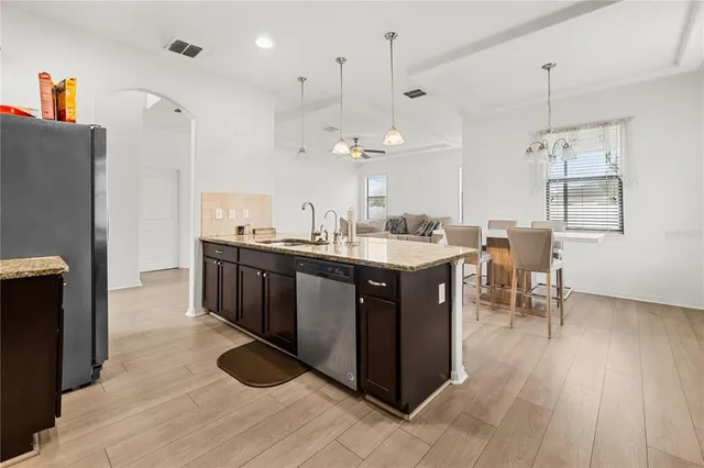 a kitchen with stainless steel appliances granite countertop a sink a stove a refrigerator and island with wooden floor