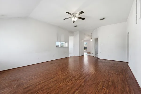 a view of an empty room with wooden floor and a ceiling fan