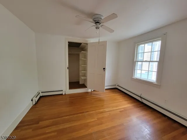 an empty room with wooden floor ceiling fan and windows