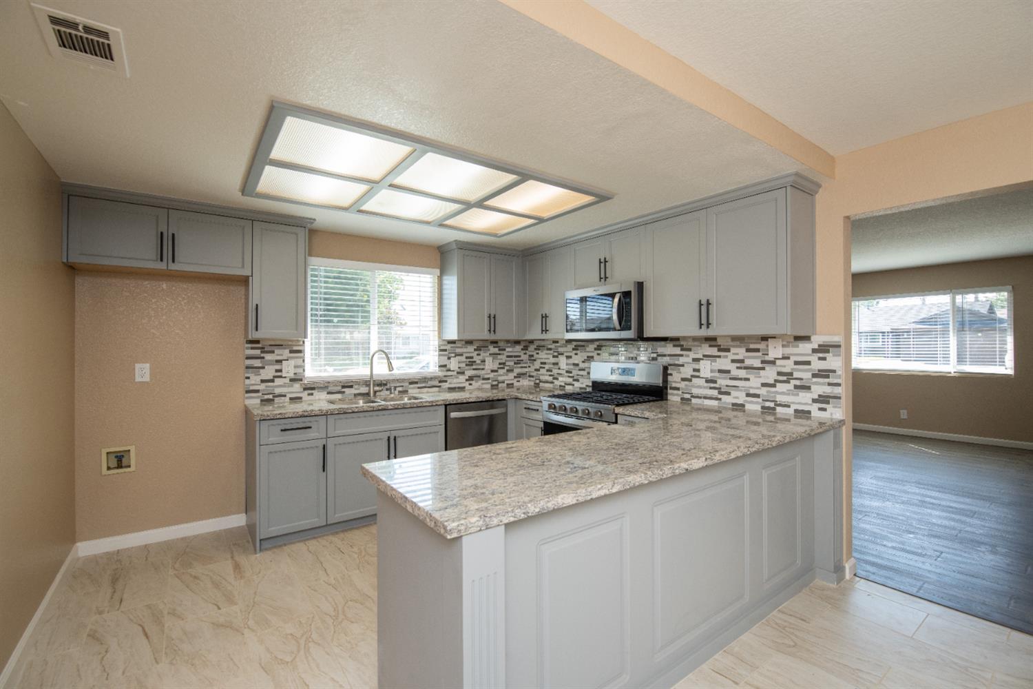 1621 Davis Street Ripon, CA 95366 - Photo 9 of 43 kitchen with gray cabinets, stainless steel appliances, a peninsula, light stone countertops, and a textured ceiling