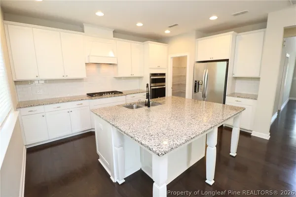 a kitchen with stainless steel appliances granite countertop a kitchen island a stove a sink a refrigerator and white cabinets with wooden floor