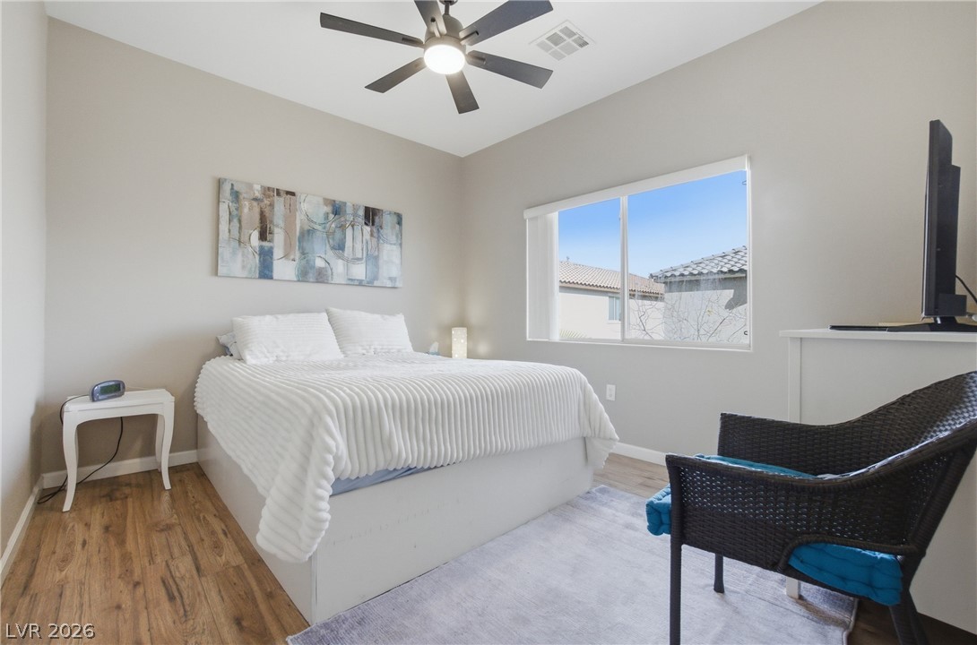 6316 Snap Ridge Street, Unit 101 North Las Vegas, NV 89081 - Photo 16 of 41 spacious primary bedroom features vaulted ceilings, a modern ceiling fan, and abundant natural light from a large window. Neutral tones and wood-look flooring create a relaxing retreat with a clean, contemporary feel.