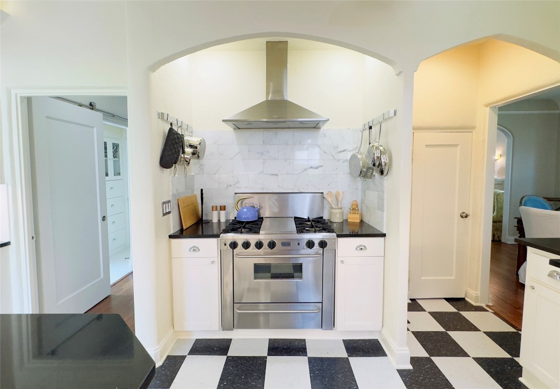 1512 Northwood Road Austin, TX 78703 - Photo 16 of 24 Kitchen featuring dark flooring, decorative backsplash, arched walkways, wall chimney exhaust hood, and white cabinets