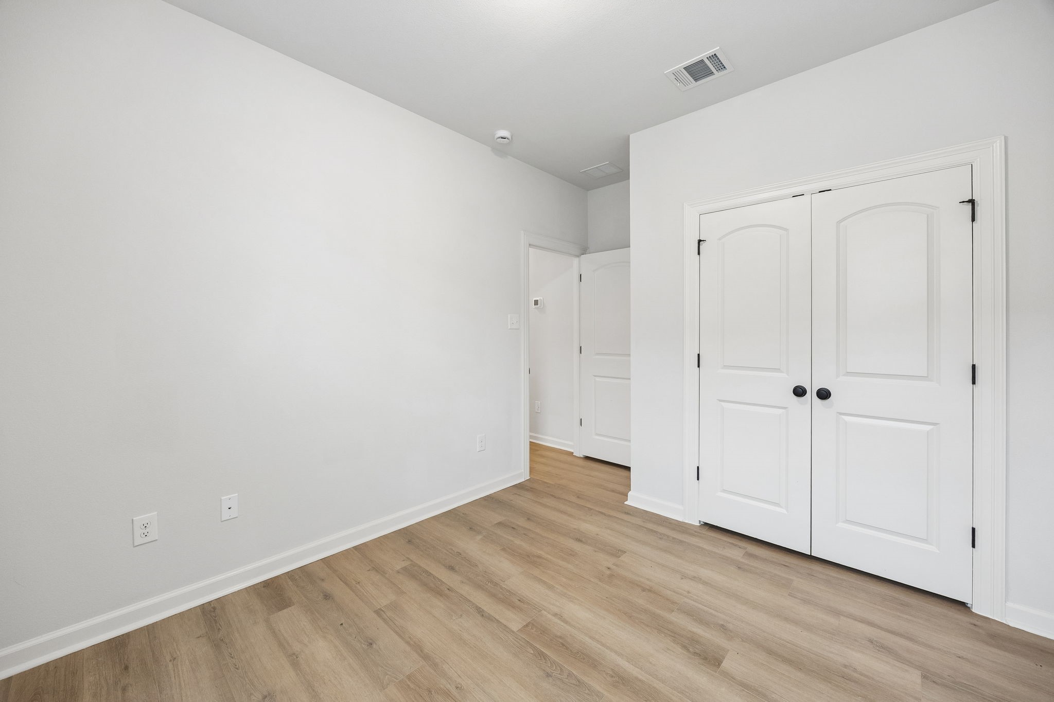 10902 Bonfire Trail Beasley, TX 77417 - Photo 18 of 36 This secondary bedroom features a clean, modern design with light-color walls and vinyl plank flooring. It includes a double-door closet and a simple white door, providing ample storage and a minimalist aesthetic.