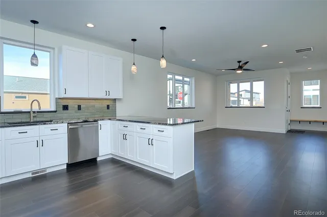 a kitchen with granite countertop white cabinets a sink a window and wooden floor
