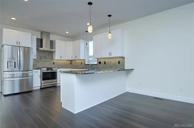 a kitchen with stainless steel appliances granite countertop a sink a stove a refrigerator and island with wooden floor