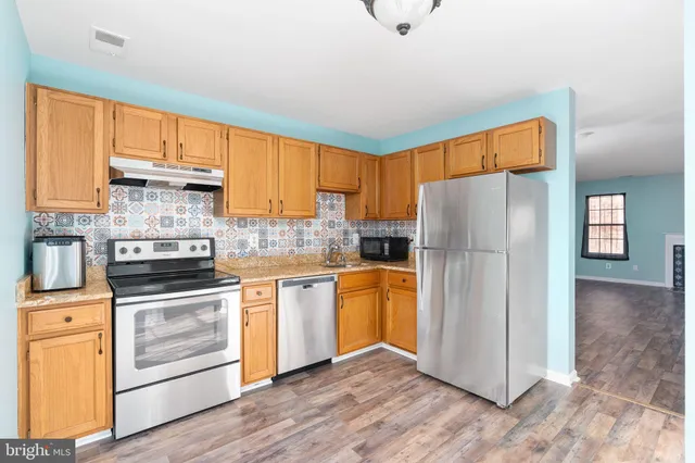 a kitchen with granite countertop stainless steel appliances a refrigerator cabinets and wooden floor