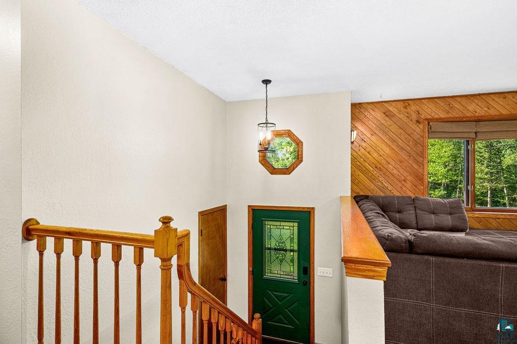 5370 Ugstad Road Hermantown, MN 55811 - Photo 27 of 68 Wood railing with balusters, green entry door with decorative glass, octagonal accent window, overhead pendant lighting, and wood-paneled wall