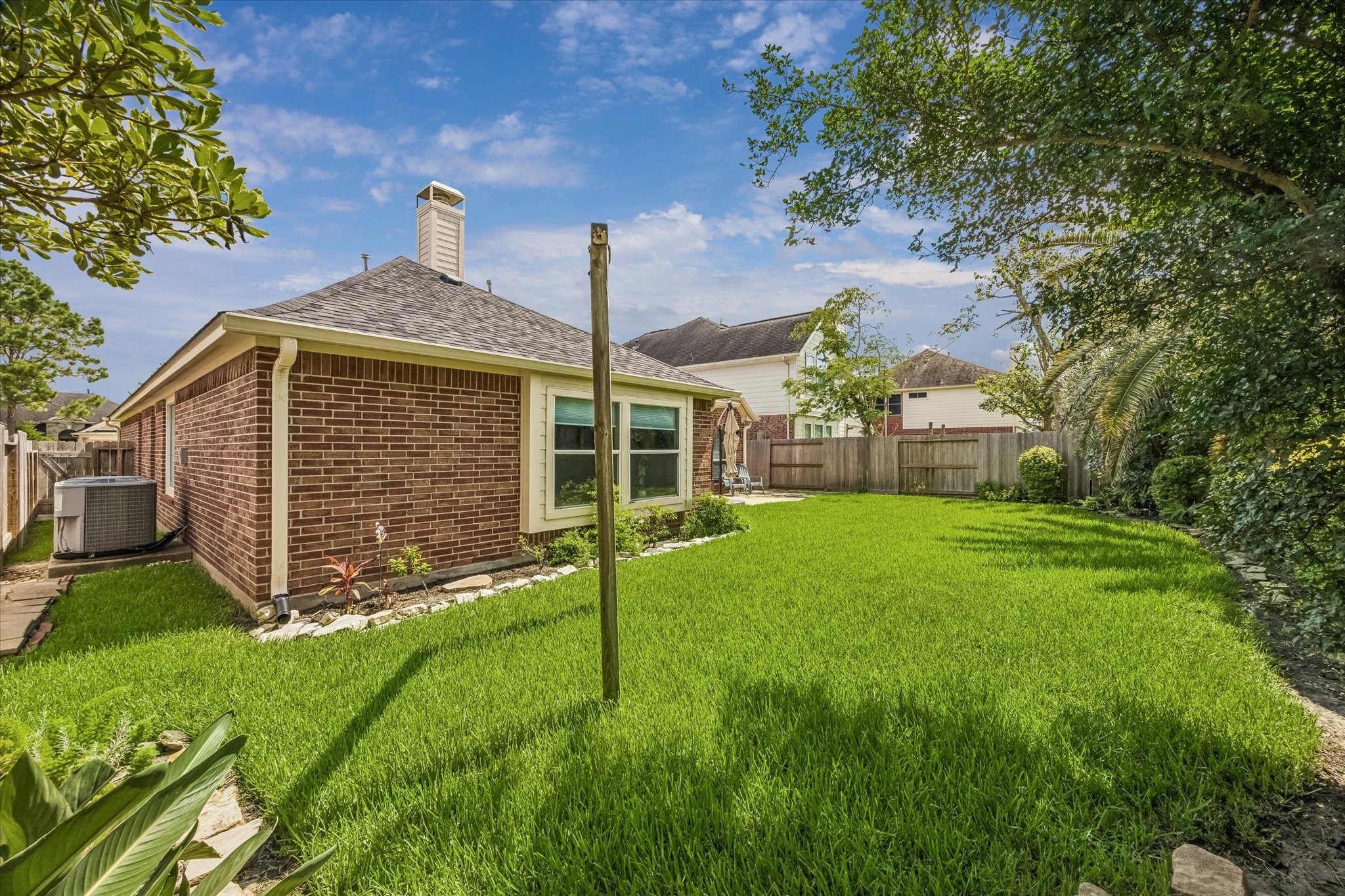 3118 Valley Court Manvel, TX 77578 - Photo 35 of 38 This photo showcases a well-maintained backyard with a lush green lawn and a brick exterior of the house. The space is bordered by a wooden fence and mature trees, offering privacy and a serene atmosphere. Perfect for outdoor activities and relaxation.