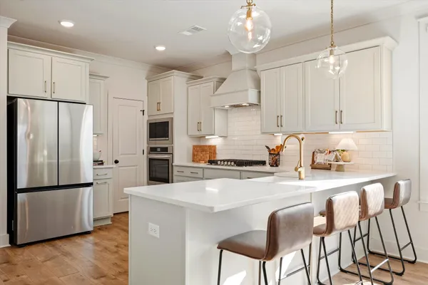 a kitchen with stainless steel appliances granite countertop a refrigerator a sink dishwasher a stove and white cabinets with wooden floor