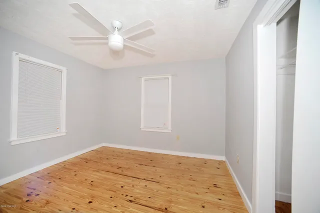 a view of an empty room with wooden floor and a ceiling fan