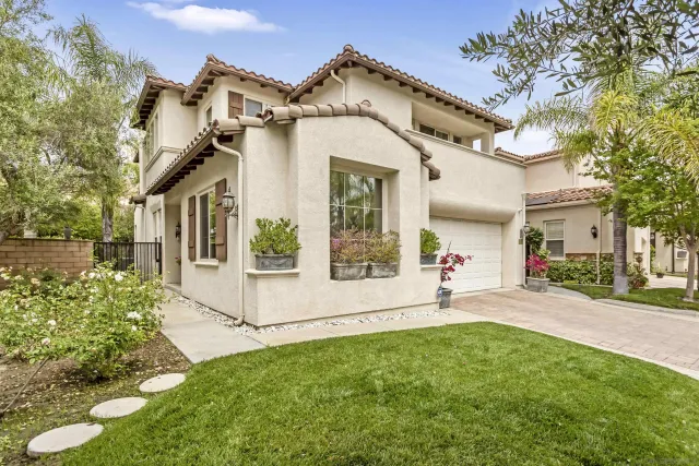 a view of a white house with a large tree and a yard with plants