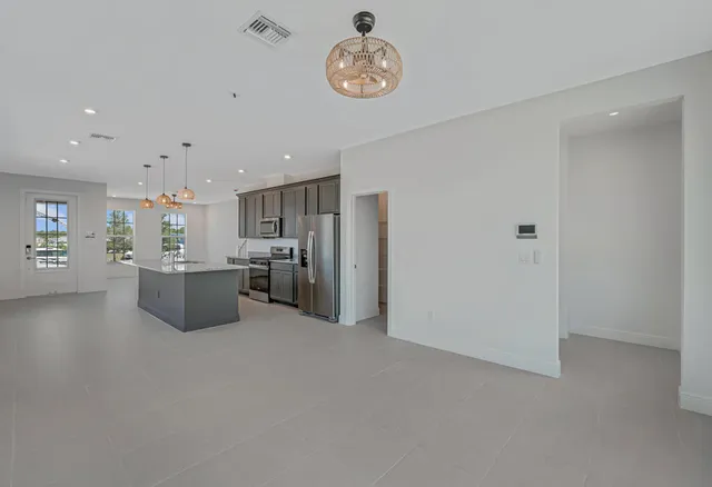 a kitchen with stainless steel appliances kitchen island granite countertop a refrigerator a oven a sink and white cabinets with wooden floor