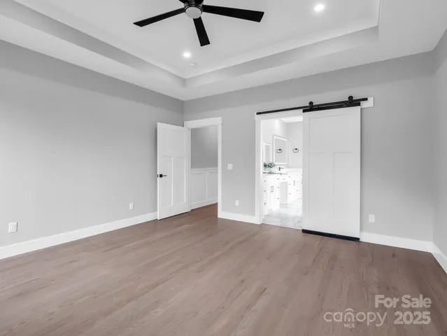 a view of an empty room with wooden floor and a ceiling fan