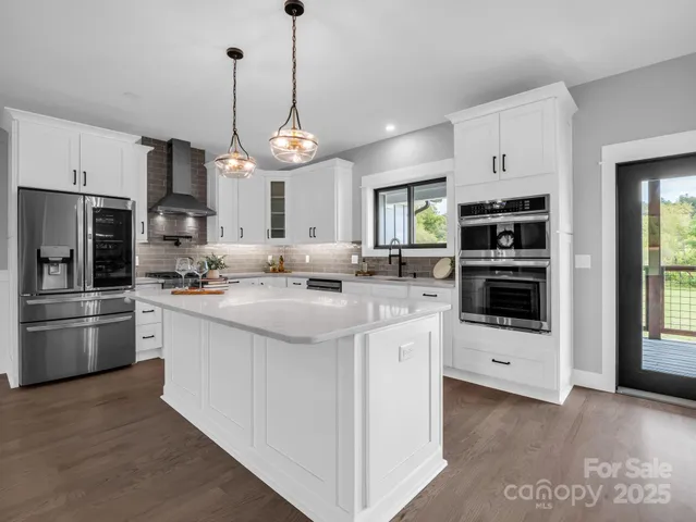 a kitchen with stainless steel appliances kitchen island granite countertop a refrigerator a oven a stove and a sink with wooden floor