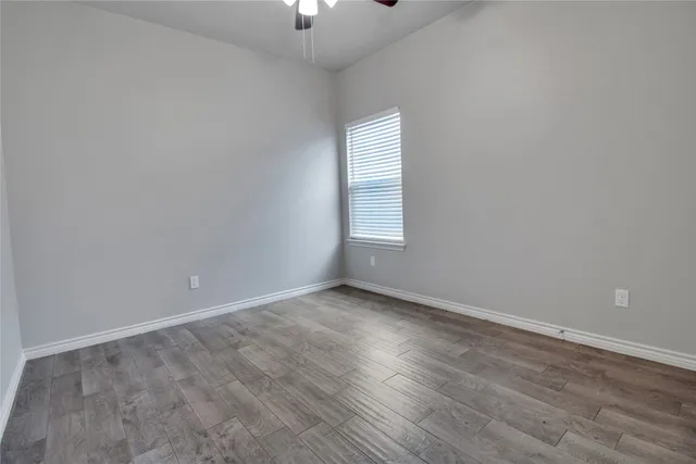 an empty room with wooden floor chandelier fan and windows