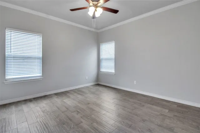 an empty room with wooden floor chandelier fan and windows