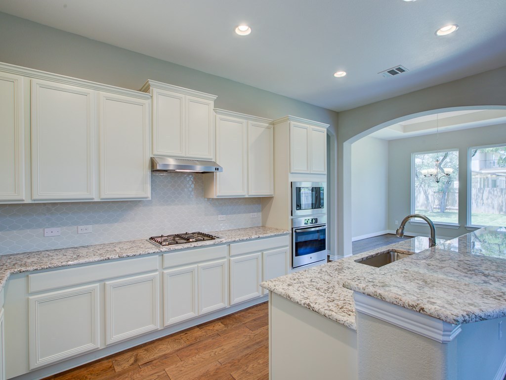 4303 Logan Ridge Drive Cedar Park, TX 78613 - Photo 3 of 24 Well-appointed kitchen featuring white cabinetry, granite countertops, wood-finish flooring, stainless steel appliances, and a gas cooktop
