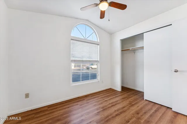 an empty room with wooden floor chandelier fan and windows