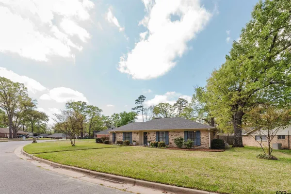 a view of a white house with a big yard and potted plants and large trees