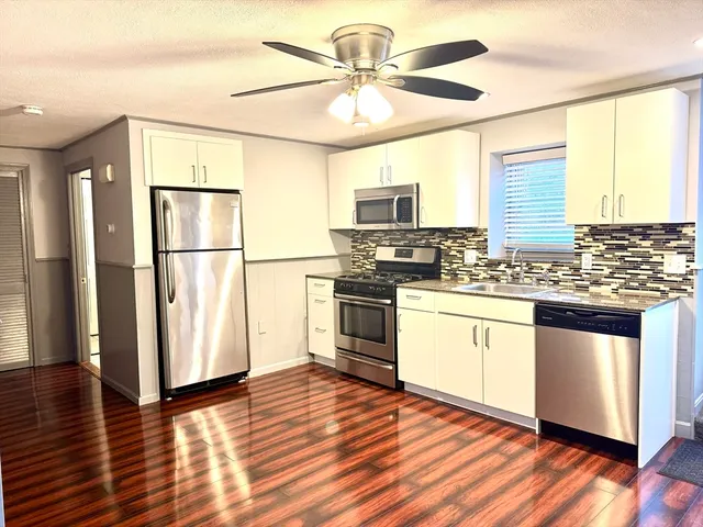 a kitchen with stainless steel appliances granite countertop a refrigerator a stove a sink and white cabinets with wooden floor