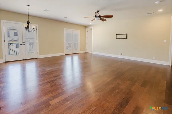 a view of an empty room with wooden floor and a ceiling fan