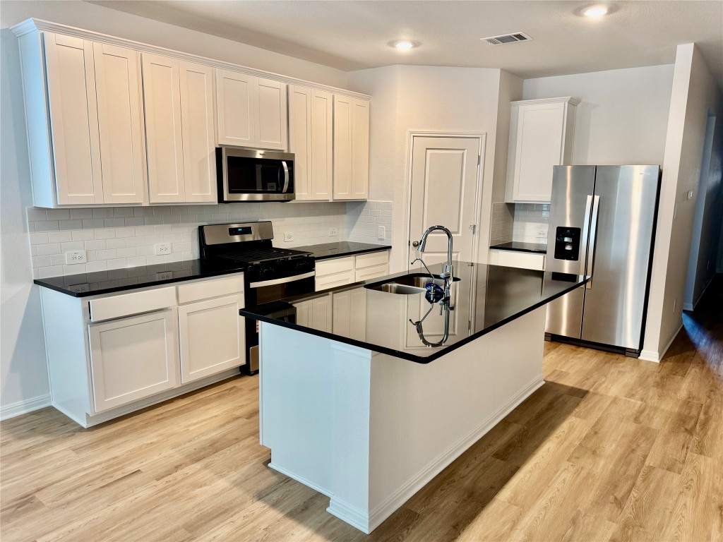 298 Texas Agate Drive Kyle, TX 78640 - Photo 2 of 7 Kitchen with appliances with stainless steel finishes, white cabinetry, a kitchen island with sink, light wood-style floors, and backsplash