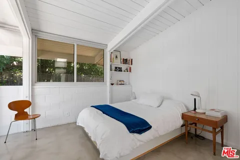 a bedroom with a bed a chair and potted plant next to a large window