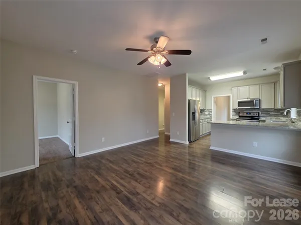 a view of an empty room and kitchen with wooden floor