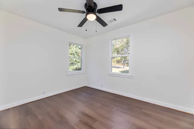an empty room with wooden floor ceiling fan and windows