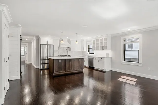 a living room with stainless steel appliances kitchen island granite countertop a refrigerator a stove a sink dishwasher and white cabinets with wooden floor