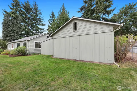 a view of a white house in front of a yard with large tree