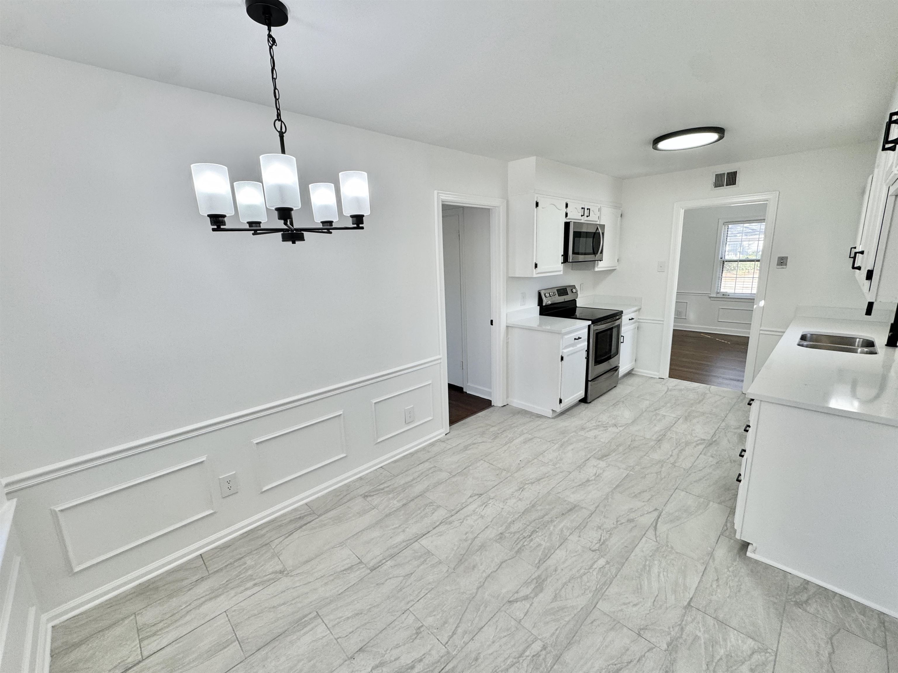 4417 Fair Meadow Road Memphis, TN 38117 - Photo 6 of 38 Kitchen featuring a decorative wall, wainscoting, white cabinetry, appliances with stainless steel finishes, and decorative light fixtures