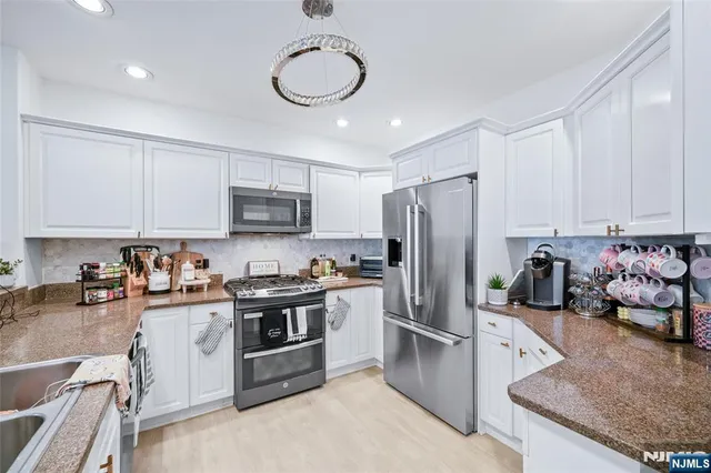 a kitchen with stainless steel appliances granite countertop a stove top oven a refrigerator a sink and dishwasher with white cabinets