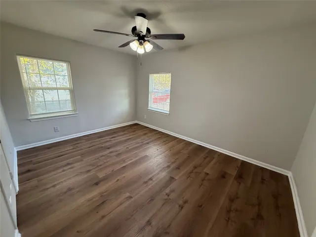 an empty room with wooden floor fan and windows
