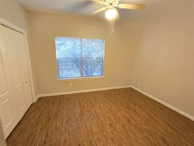 an empty room with wooden floor fan and windows
