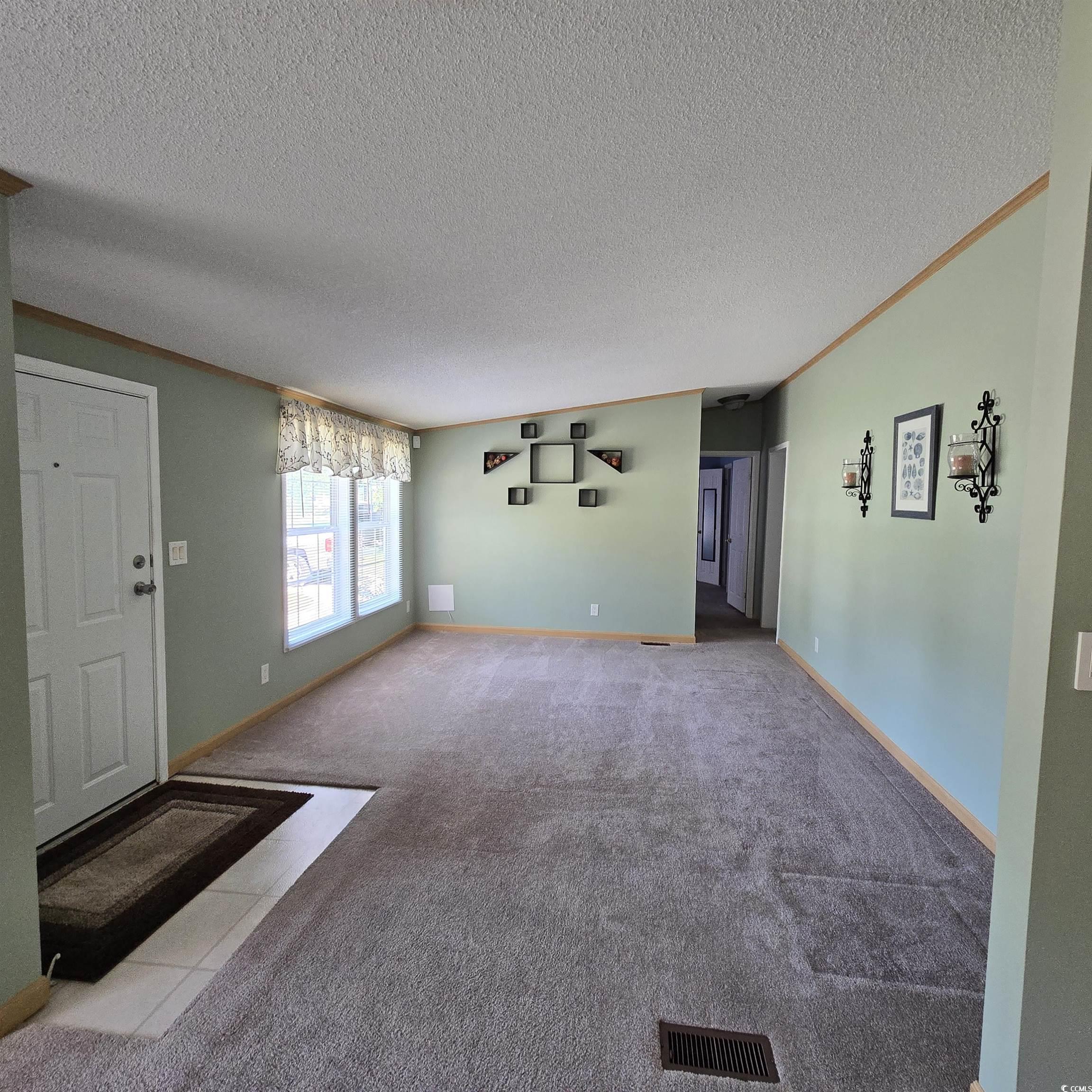 34 Talon Circle Murrells Inlet, SC 29576 - Photo 14 of 40 Unfurnished living room featuring carpet flooring, a textured ceiling, crown molding, and tile patterned flooring