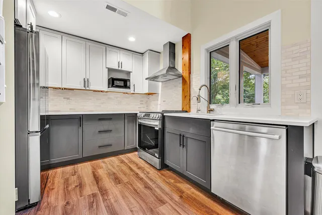 a kitchen with stainless steel appliances granite countertop a refrigerator a sink dishwasher a stove and white countertops with wooden floor