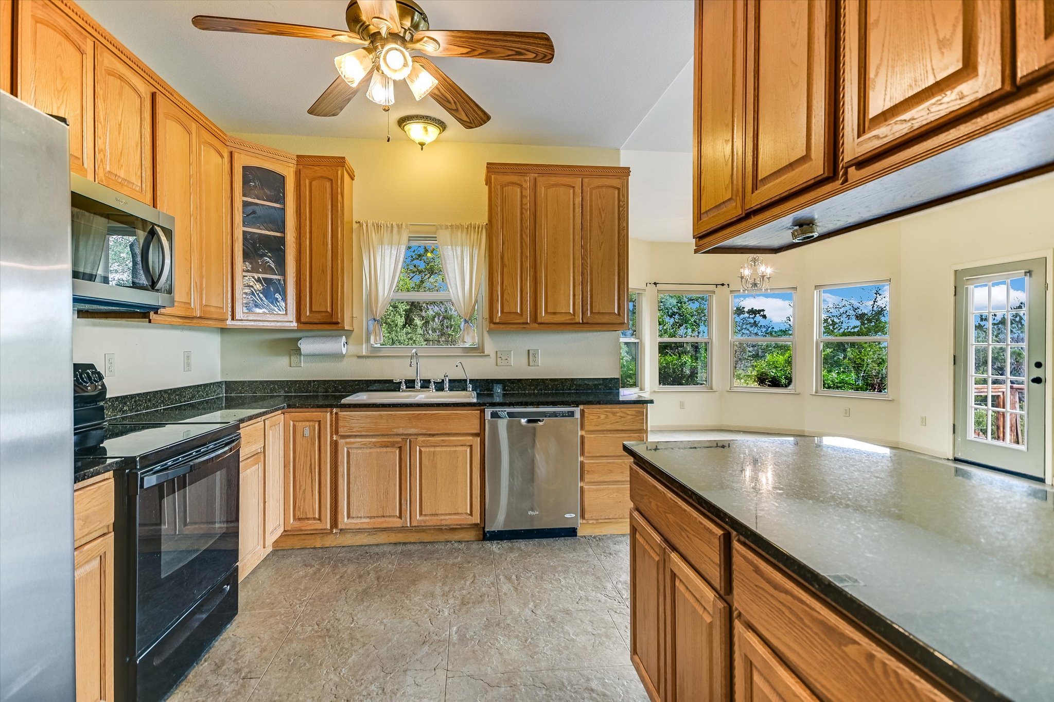 700 Cliffside Road Wimberley, TX 78676 - Photo 6 of 22 Kitchen featuring wood cabinetry, black countertops, stainless steel appliances, and a ceiling fan with integrated lighting