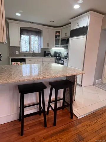 a kitchen with granite countertop wooden floor white cabinets and refrigerator