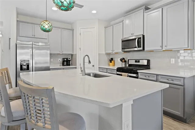 a kitchen with stainless steel appliances a sink a stove a microwave a refrigerator a white table and chairs