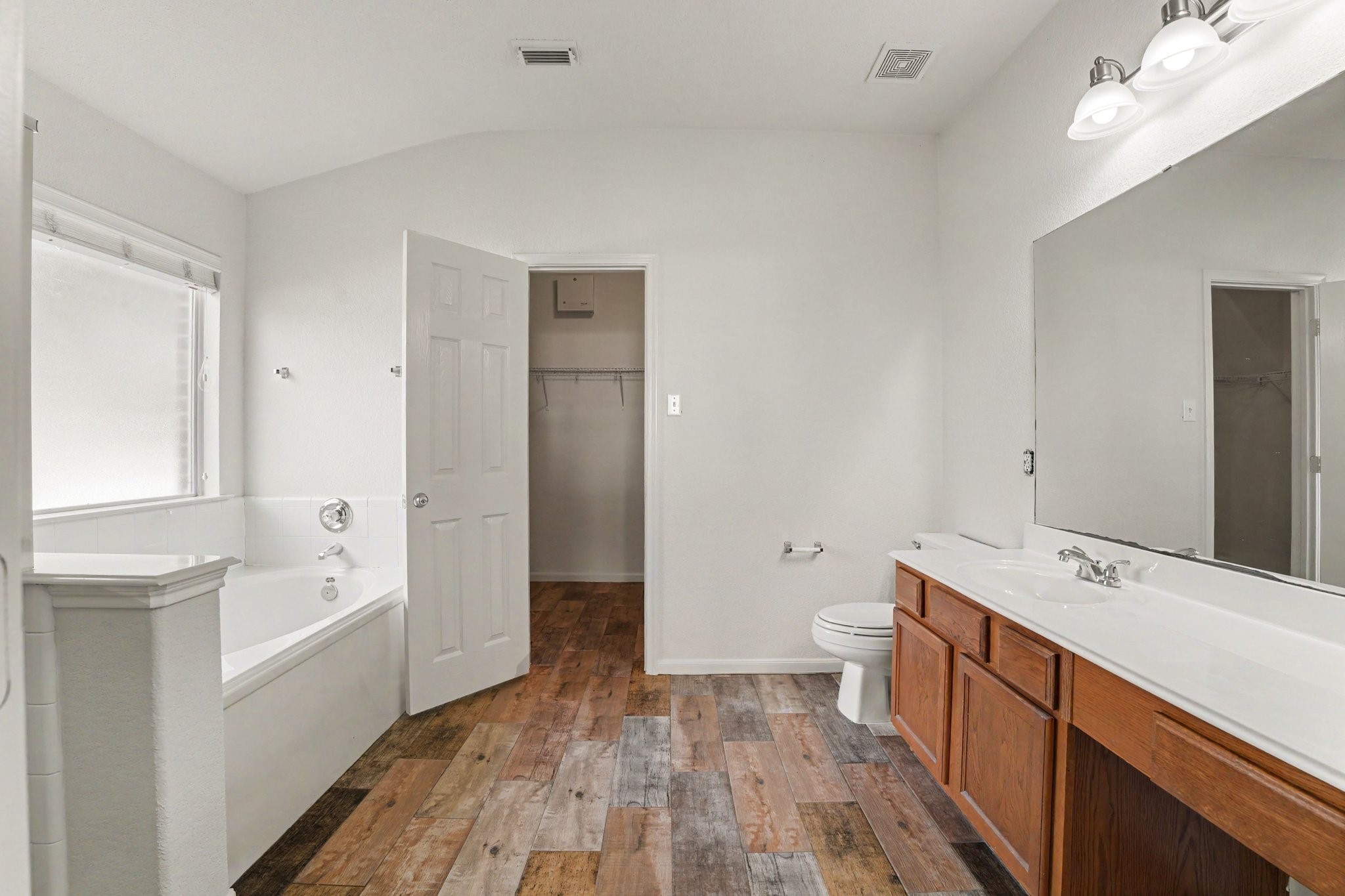 21427 Blooming Rock Lane Spring, TX 77379 - Photo 20 of 32 This spacious bathroom features a large soaking tub, dual sinks with a wide mirror, and warm wood-look flooring. There is ample natural light from a large window and access to a walk-in closet.