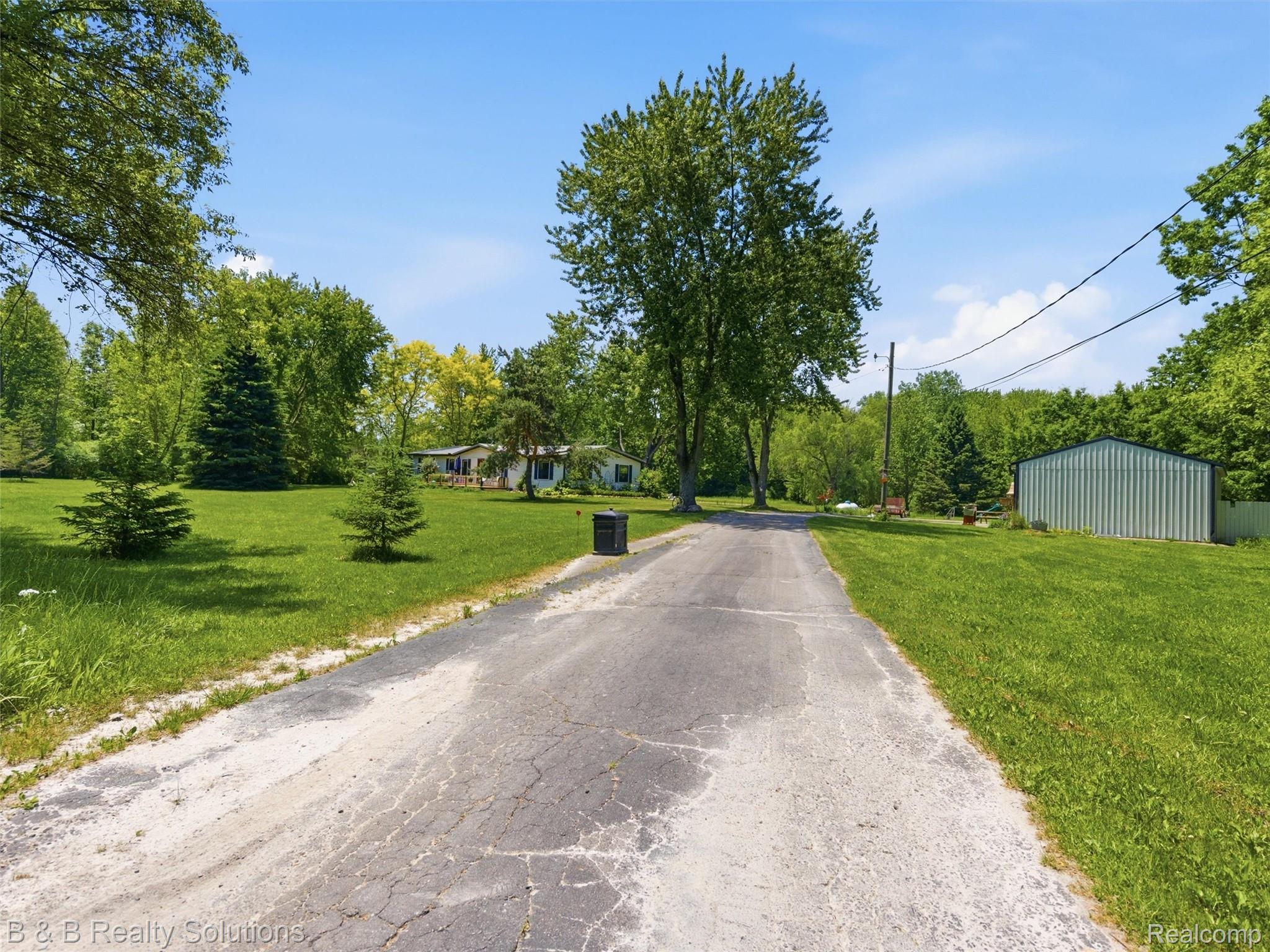 60455 Bates Road New Haven, MI 48048 - Photo 57 of 58 Expansive green lawn with mature trees and a paved driveway leading to a metal-sided outbuilding