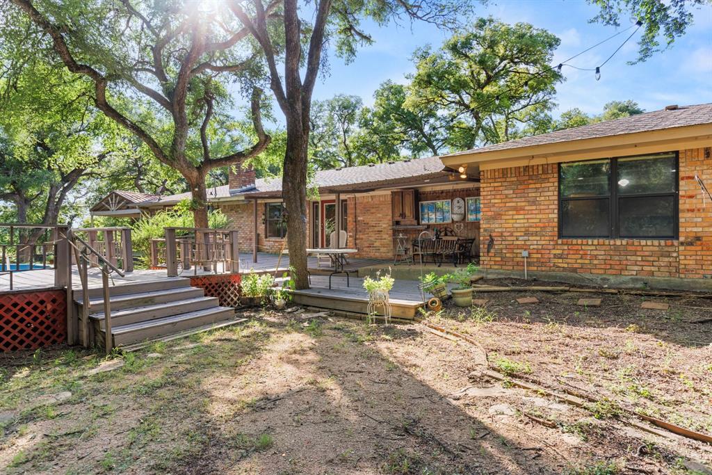 13539 Chapel Road Lorena, TX 76655 - Photo 33 of 37 Expansive backyard featuring a multi-level wood deck with lattice skirting, mature trees, and a brick exterior home with a covered patio area