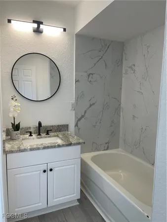 a bathroom with a granite countertop sink a mirror a bathtub and shower
